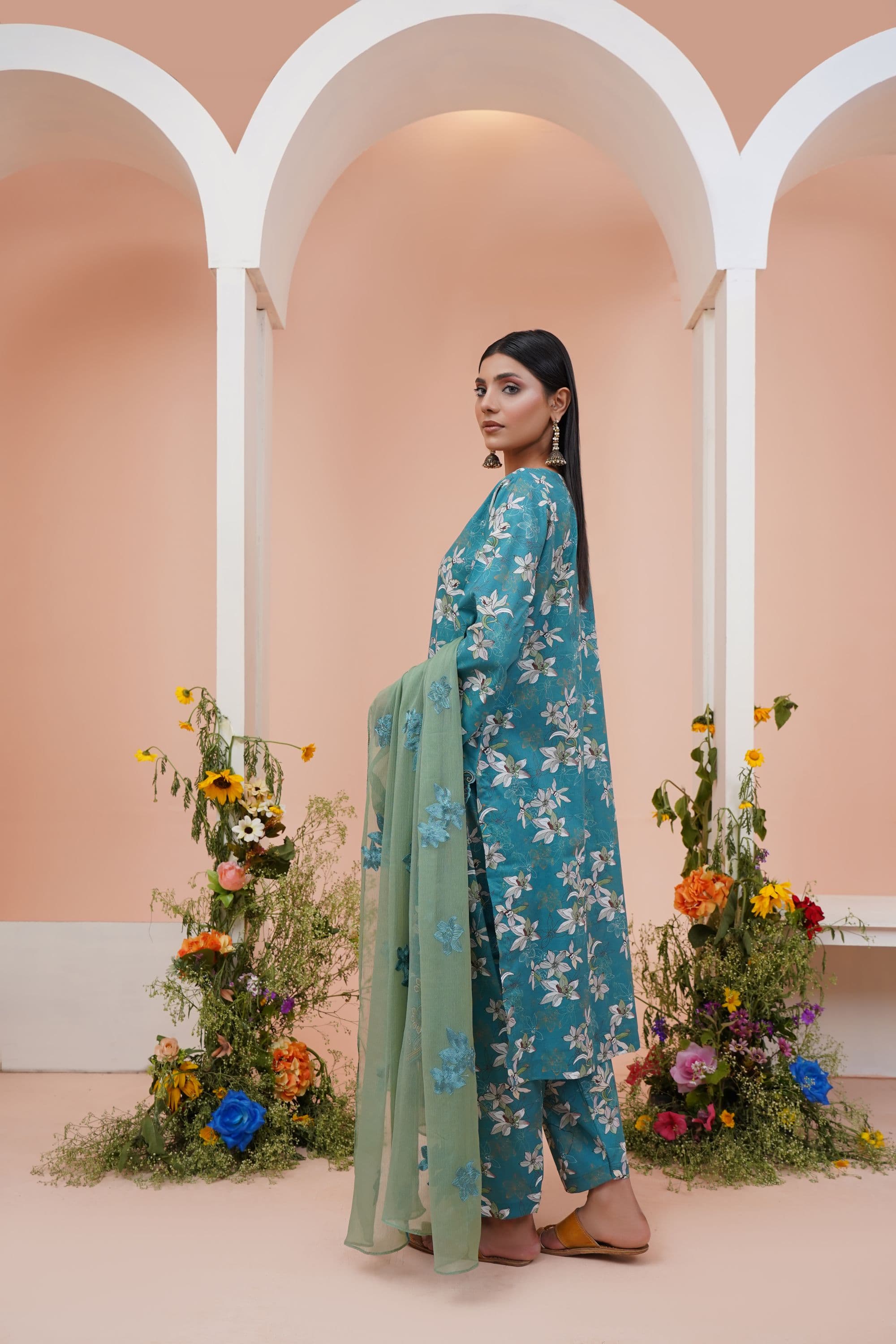 Woman in a teal floral lawn kurta with a green dupatta between white arches and flower arrangements