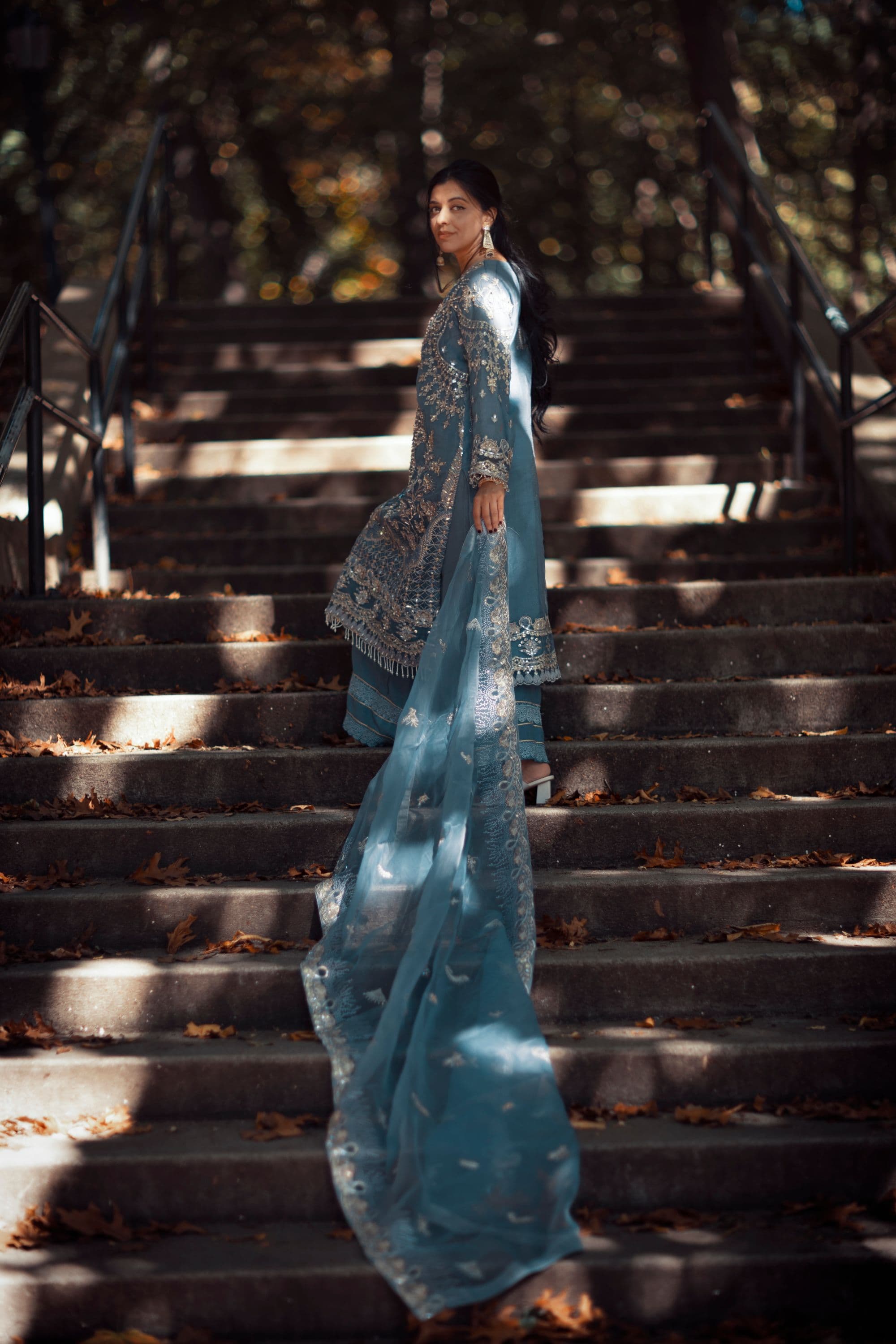 Woman in a blue embroidered formal suit with a long flowing dupatta standing on stone steps