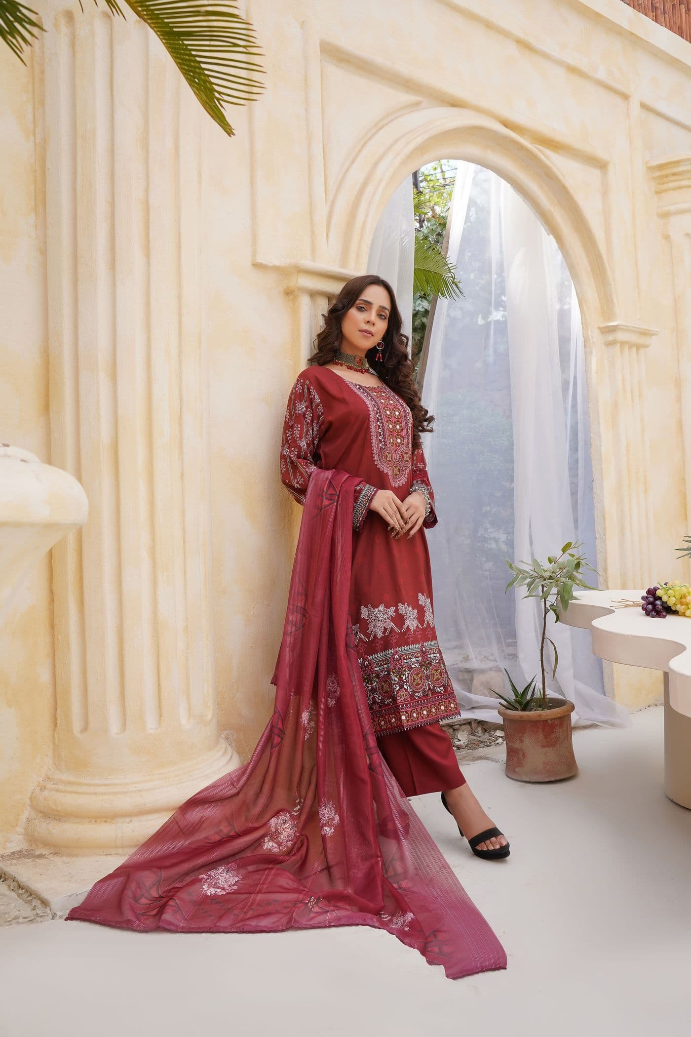 Woman in a red embroidered kurta set with a long red dupatta in a sandstone arched courtyard