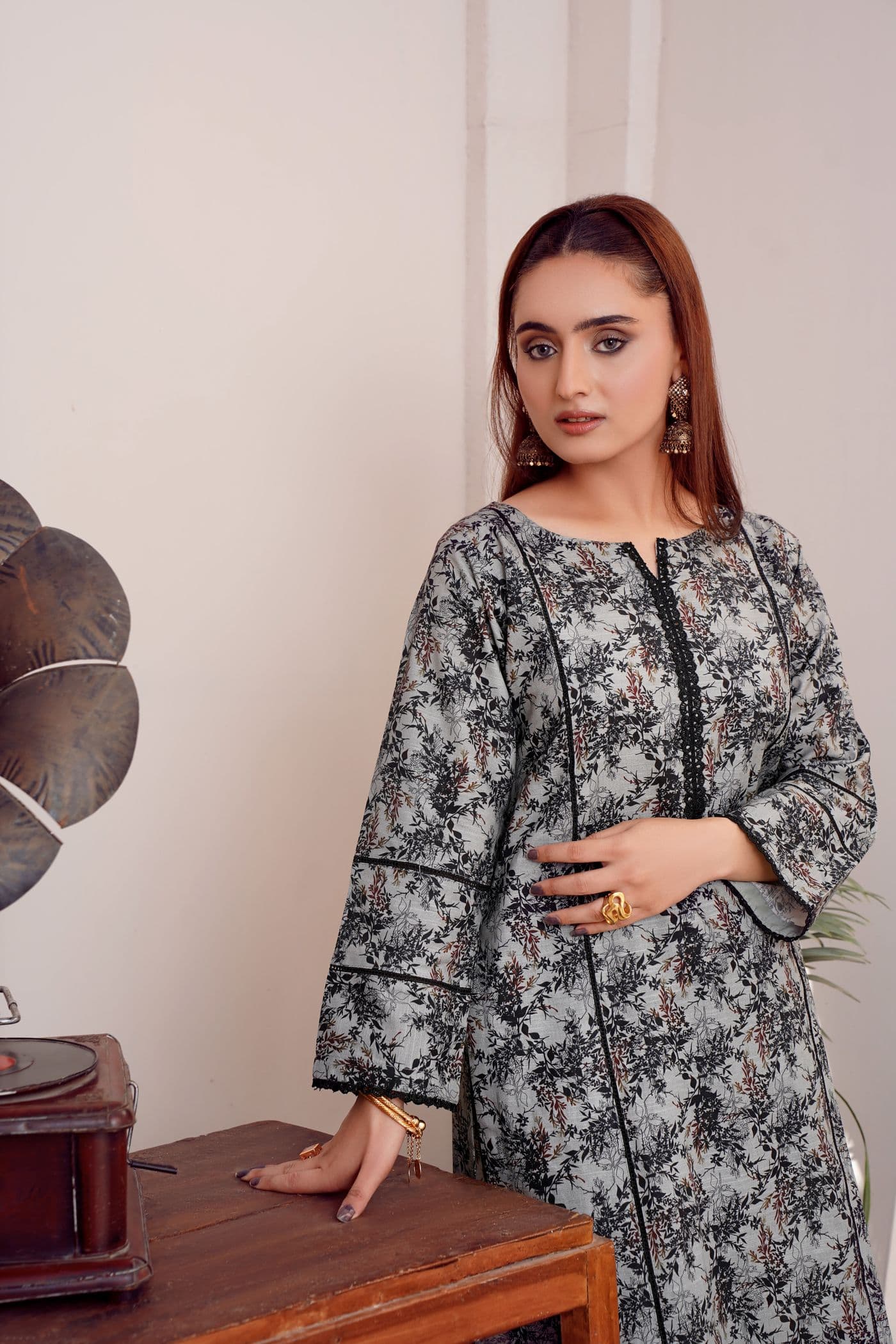 Woman in a grey floral printed lawn kurta with black piping standing beside a wooden table